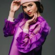 Retrato de mujer hermosa en vestido púrpura de moda y sombrero mirando a la cámara sobre fondo negro