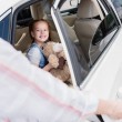 Enfoque selectivo de niño sonriente con oso de peluche mirando a la madre abriendo la puerta del coche
