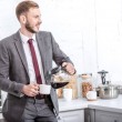 Guapo hombre de negocios vertiendo café filtrado en taza en la cocina y mirando hacia otro lado