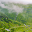 Hermoso paisaje y vista panorámica de Noruega, verdes colinas y montañas en un día nublado. paisaje verde de colinas y montañas parcialmente cubiertas de niebla. Granja y cabañas en un río glaciar